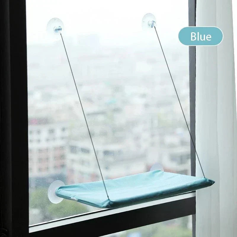 Blue cat window perch attached to a window with strong suction cups, providing a cozy spot for cats to sunbathe and enjoy the view.